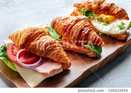 Croissant sandwich variety. Various stuffed croissants on a wooden cutting board 109828948