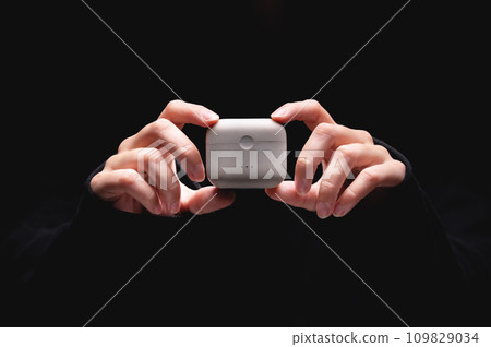 close-up of young woman hands holding wireless headphones charger. case for vacuum headphones on a black background close-up of young woman hands holding wireless headphones charger. case for vacuum headphones on a black background 109829034