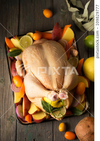 A large chicken stuffed with an apple with vegetables and citrus fruits, top view A large chicken stuffed with an apple with vegetables and citrus fruits, top view 109829777