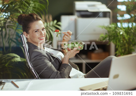 happy 40 years old woman worker in green office eating salad 109831691