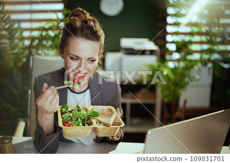 smiling business owner woman in green office eating salad smiling business owner woman in green office eating salad 109831701