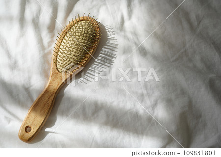 Wooden hairbrush on white bed background with shadows from window Wooden hairbrush on white bed background with shadows from window 109831801