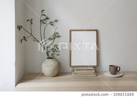 Spring, Easter breakfast still life. Elegant Scandinavian living room, home office. Cup of coffee, books. Empty wooden picture frame mockup on desk, table. Vase with willow tree branches, catkins. 109831889