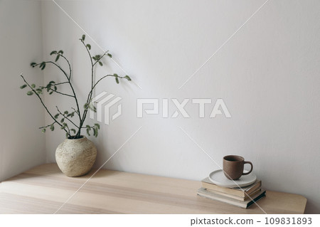 Minimal Scandinavian living room interior.. Cup of coffee, books on wooden table. Vase with willow tree branches, catkins. Elegant Scandi working space, home office. Blank beige wall background 109831893