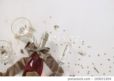 New years Eve holiday corner, banner. Bottle of champagne rose wine, glasses. Golden bow, star shape confetti isolated on white table background. Birthday, party celebration. Alcohol drink. Flat lay 109831894