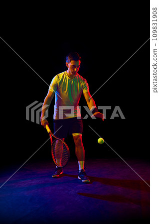 Warming up. Man, athlete in his 30s playing tennis, practicing against dark background in neon light 109831908