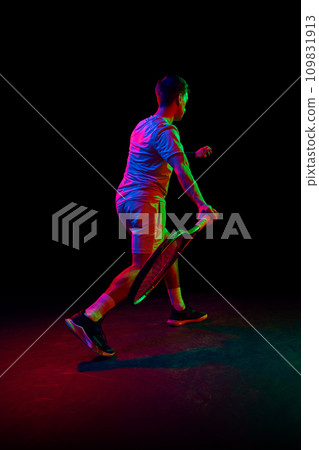 Young man, tennis player during game, playing, practicing against dark background in neon light 109831913