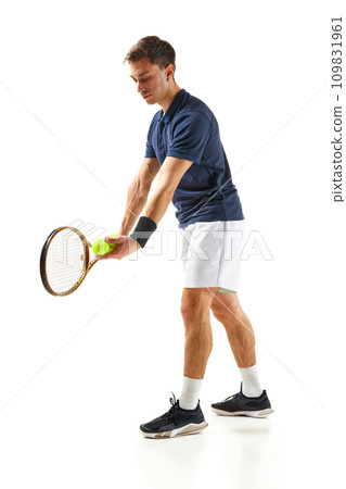 Concentrated man in his 30s, tennis player in blue shirt standing with racket, serving ball isolated over white background Concentrated man in his 30s, tennis player in blue shirt standing with racket, serving ball isolated over white background 109831961