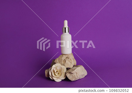 Glass dropper bottle with cosmetic oil, essential or serum staying on stone stand with dry flower on violet background. Herbal homeopathic products Natural organic spa cosmetics Glass dropper bottle with cosmetic oil, essential or serum staying on stone stand with dry flower on violet background. Herbal homeopathic products Natural organic spa cosmetics 109832052