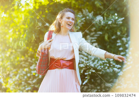smiling elegant woman in pink dress and white jacket in city 109832474