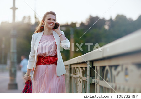 smiling female in dress and jacket in city talking on phone smiling female in dress and jacket in city talking on phone 109832487