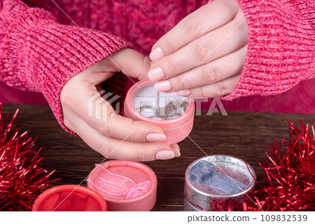 Female hands with pink manicure take out a chain from a round gift box. Female hands with pink manicure take out a chain from a round gift box. 109832539