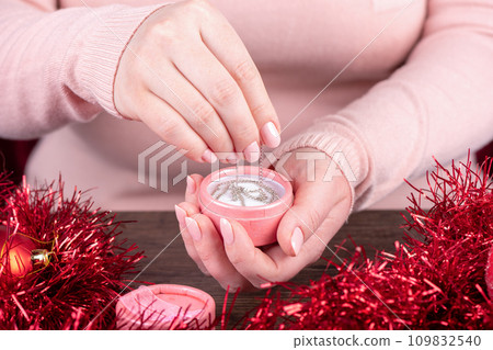 A young woman takes a chain out of a pink gift box. 109832540