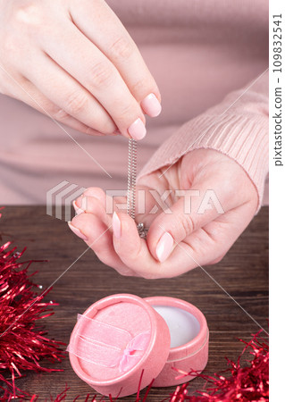 Chain in female hands with pink manicure, gift box on a wooden background. 109832541