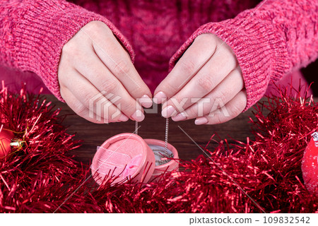 Female hands with natural pink manicure take out a chain from a pink gift box. 109832542