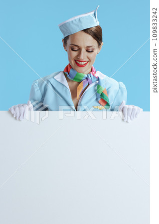 happy female flight attendant on blue showing blank board 109833242