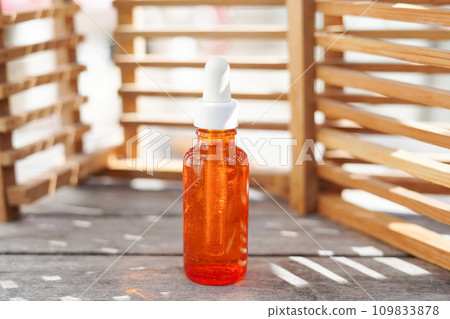 Red glass Bottle Mock-Up. cosmetic oil bottle with shadows from wooden wall, Body treatment and spa. Natural beauty products. Eco serum. Anti-cellulite massage oil 109833878