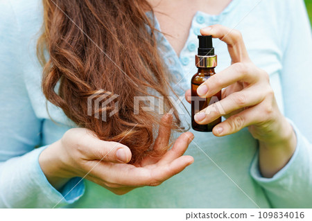 Young woman applying natural organic essential oil on hair. spa and beauty rituals. Skin care Young woman applying natural organic essential oil on hair. spa and beauty rituals. Skin care 109834016