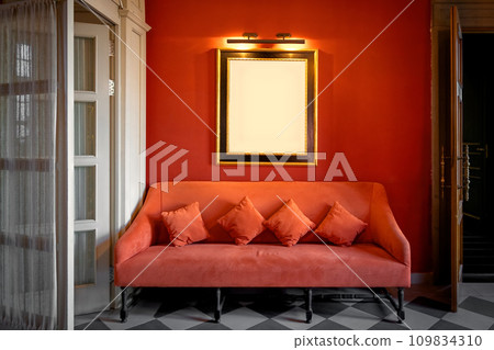 Mockup with a frame for a picture or photo on a red wall above a sofa in a classic interior 109834310