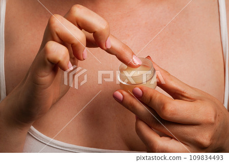 woman holds cosmetic cream in hands against her body, natural skin care products 109834493