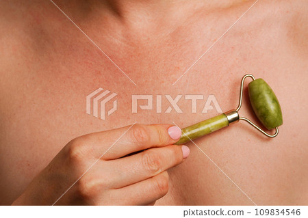 Woman doing self massage with green quartz face roller, gua sha, skin care 109834546