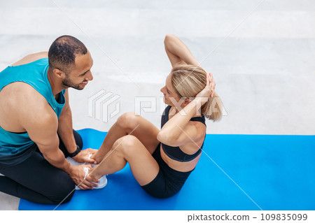 Woman with blonde hair in excellent shape doing sit-ups with her boyfriend, 109835099
