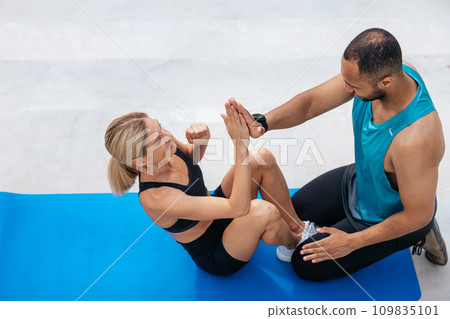 Fit woman doing sit-up with with personal trainer. Fit woman doing sit-up with with personal trainer. 109835101