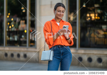 Adult woman staying on street holding phone in hands. 109835499