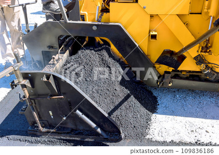 An asphalt paver lays new bitumen asphalt on top of gravel base during construction highway 109836186