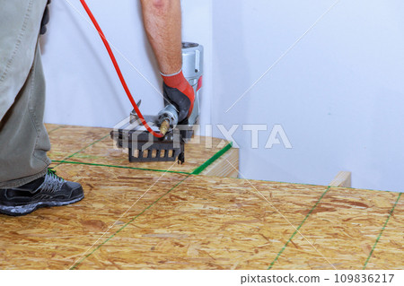 Installing wooden plywood floor in new home using an air nail gun Installing wooden plywood floor in new home using an air nail gun 109836217