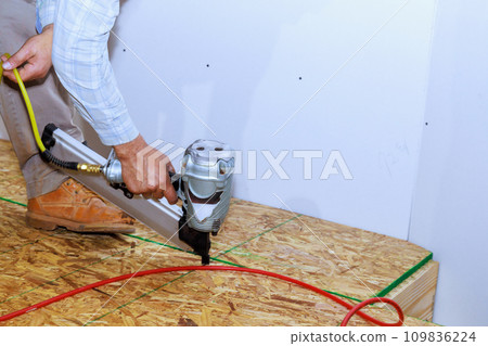 Installation of wooden plywood for floors of new home with an air nail gun 109836224