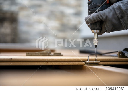 Battery screwdriver fixating screws in plastic distance marker for wooden outside patio 109836681