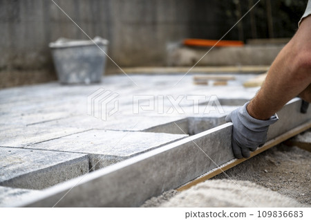 Male hands measuring and leveling sand and cement tiles for precise pavement of the outside patio Male hands measuring and leveling sand and cement tiles for precise pavement of the outside patio 109836683