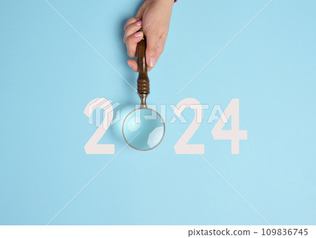 A female hand holds a magnifying glass and the inscription 2024 A female hand holds a magnifying glass and the inscription 2024 109836745