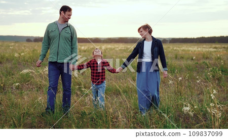 Loving parents hold son hands in field with growing plants in cloudy weather Loving parents hold son hands in field with growing plants in cloudy weather 109837099
