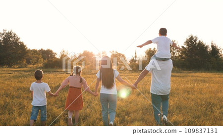 Son sits on father shoulders while family walks with across field at sunset 109837131