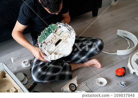 Repair of a robot vacuum cleaner that is clogged with dirt and wool. A male repairman holds a disassembled robot vacuum cleaner. the concept of repairing home electronics. 109837848