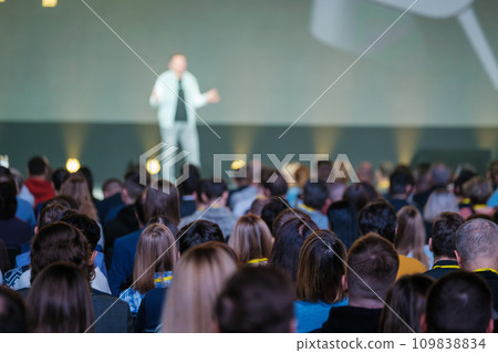 Back view of businesspeople listening to male speaker on stage during global presentation at conference hall Back view of businesspeople listening to male speaker on stage during global presentation at conference hall 109838834