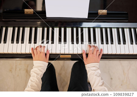 Top view of a child student, future musician pianist touching the white keys with his fingers, playing grand piano Top view of a child student, future musician pianist touching the white keys with his fingers, playing grand piano 109839827