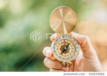 A close-up of a hand clutching a compass in the heart of a green forest. This image leaves space for text and signifies travel lifestyle and the strategic management of a thriving business. A close-up of a hand clutching a compass in the heart of a green forest. This image leaves space for text and signifies travel lifestyle and the strategic management of a thriving business. 109839968