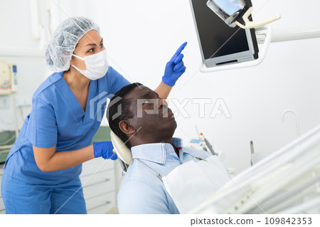 Man sitting on dental chair, female dentist pointing at display 109842353