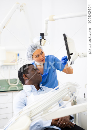 Woman dentist pointing at display to show information to patient Woman dentist pointing at display to show information to patient 109842404