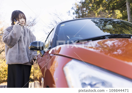 A young woman parked in a parking lot and contacted by smartphone. Image of a car malfunctioning. 109844471