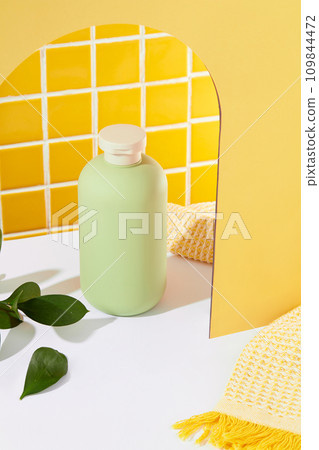 Close up of a bottle of shower gel without a label and green leaves stand out on the white table. Take care for body with safe products. Bathroom space. Close up of a bottle of shower gel without a label and green leaves stand out on the white table. Take care for body with safe products. Bathroom space. 109844472