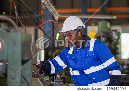 Male African American workers wearing uniform safety and hardhat working an iron cutting machine. 109844994