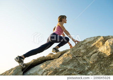 Woman hiker climbing steep big rock on a sunny day. Young female climber overcomes difficult climbing route. Active recreation in nature concept. Woman hiker climbing steep big rock on a sunny day. Young female climber overcomes difficult climbing route. Active recreation in nature concept. 109845026