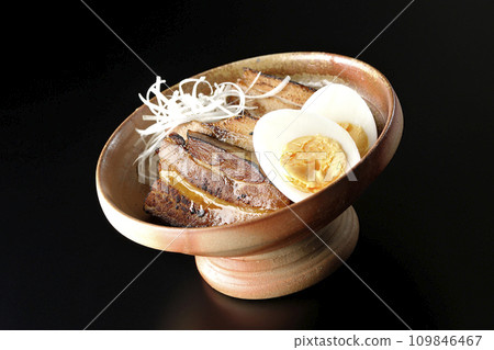 Thickly sliced char siu topped with white onion and boiled egg photographed against a black background 109846467