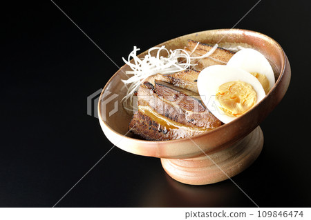 厚切的叉燒，上面放著白洋蔥和煮雞蛋，在黑色背景下拍照 109846474