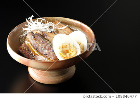 Thickly sliced char siu topped with white onion and boiled egg photographed against a black background 109846477
