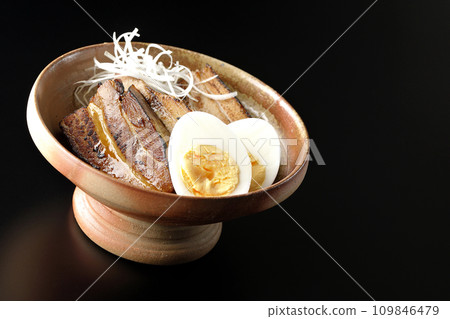 厚切的叉燒，上面放著白洋蔥和煮雞蛋，在黑色背景下拍照 109846479